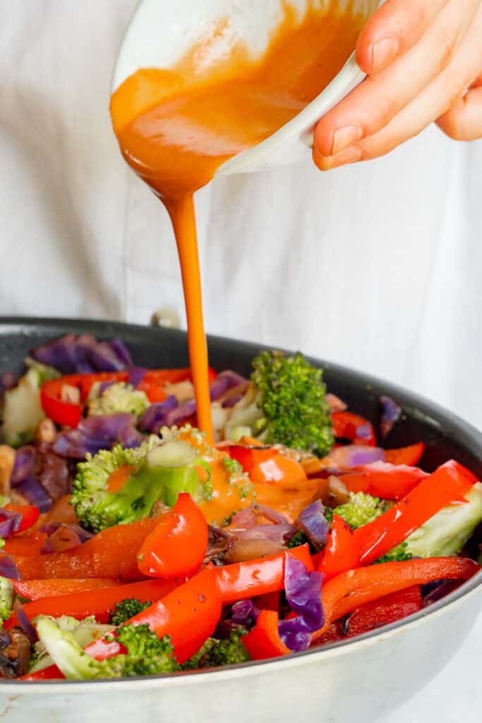 Pouring Hoisin sauce into stir-fry pan filled with vegetables.