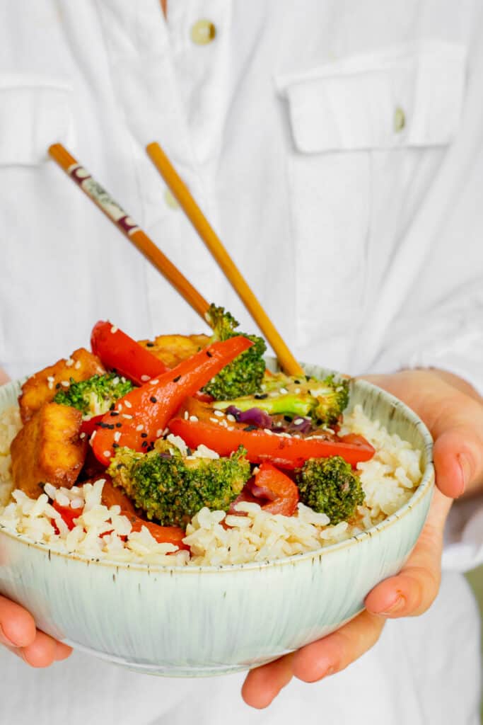 Woman holding bowl of Crispy Tofu Hoisin Stir-fry. Vegan, GF & Healthy! Georgie Eats.