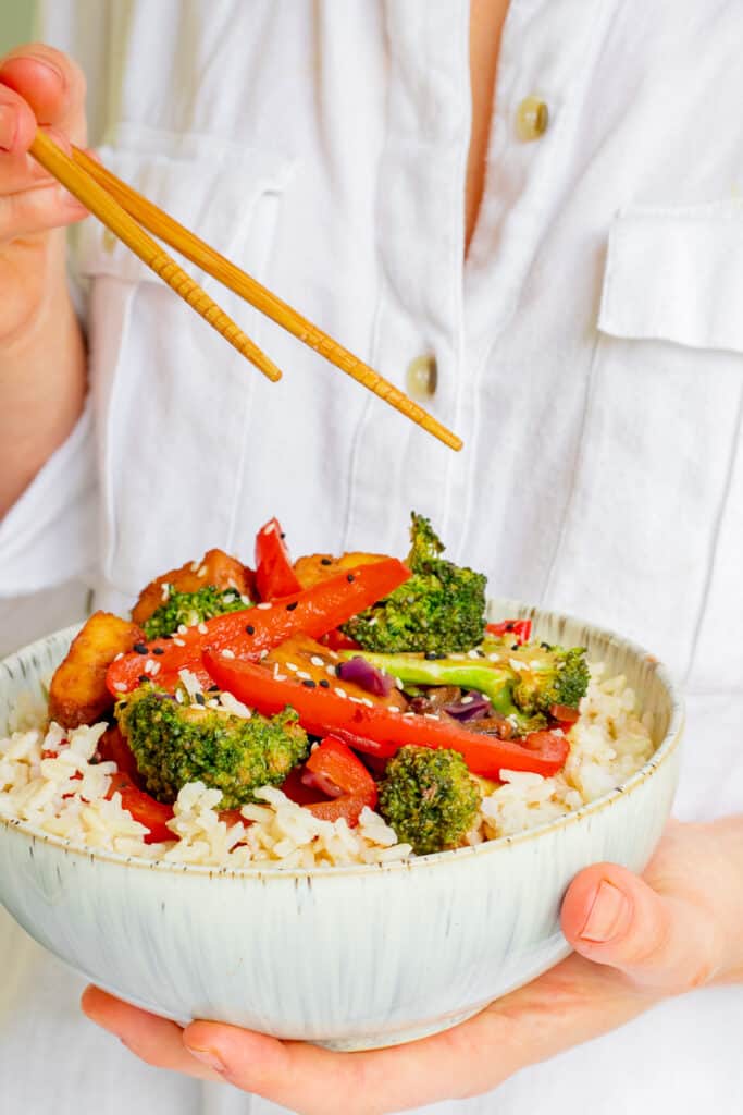 Woman holding bowl of Crispy Tofu Hoisin Stir-fry. Vegan, GF & Healthy! Georgie Eats.