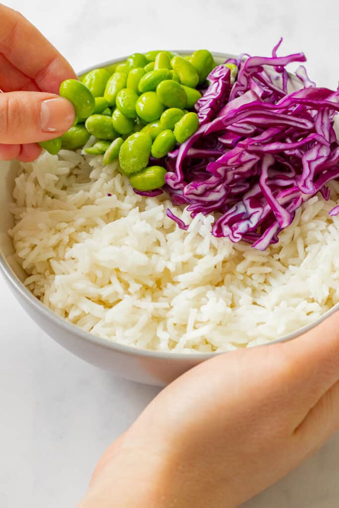 Rice and red cabbage being topped with edamame beans.