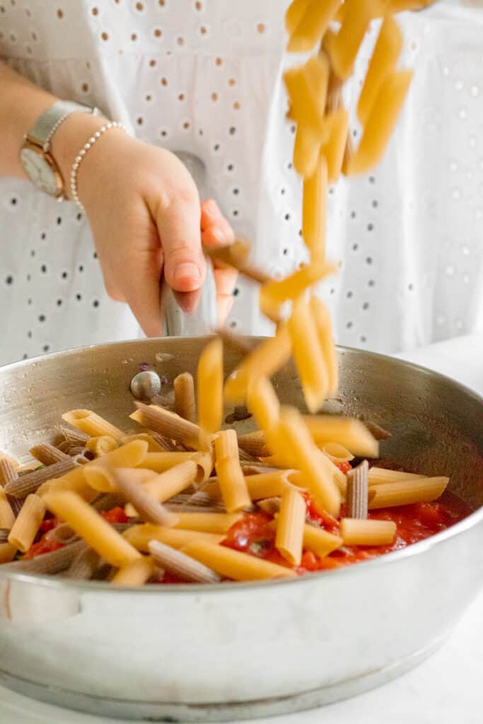 Adding the pasta into the pasta sauce.