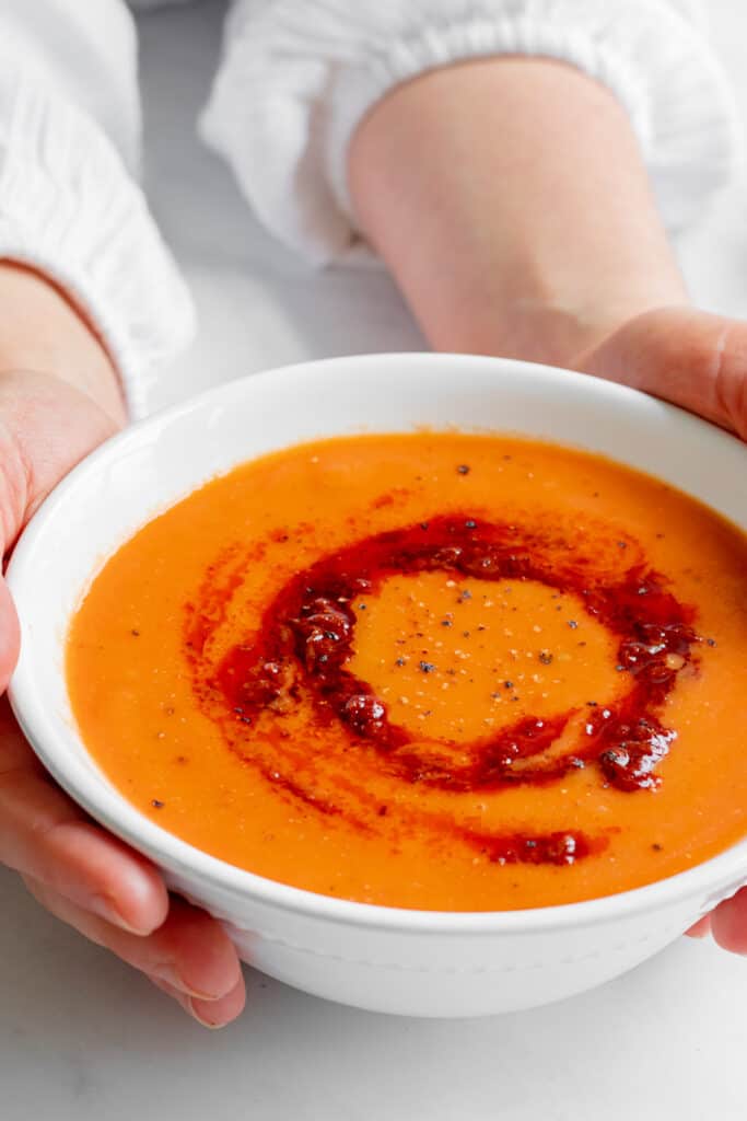Holding a bowl of Spicy Roasted Tomato & Harissa Soup - Vegan, GF & Healthy! Georgie Eats