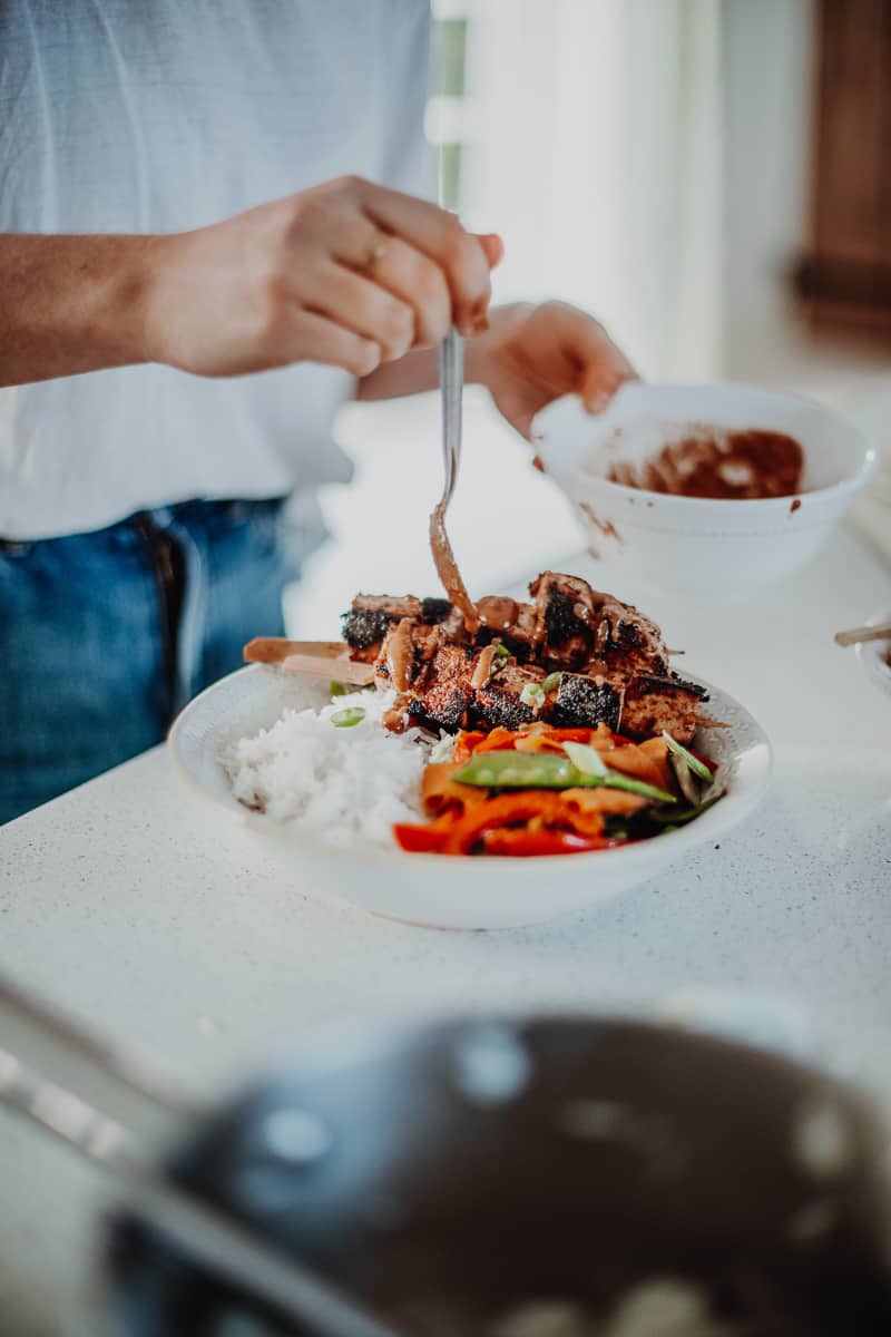 Drizzling the satay sauce over the satay tofu skewers.