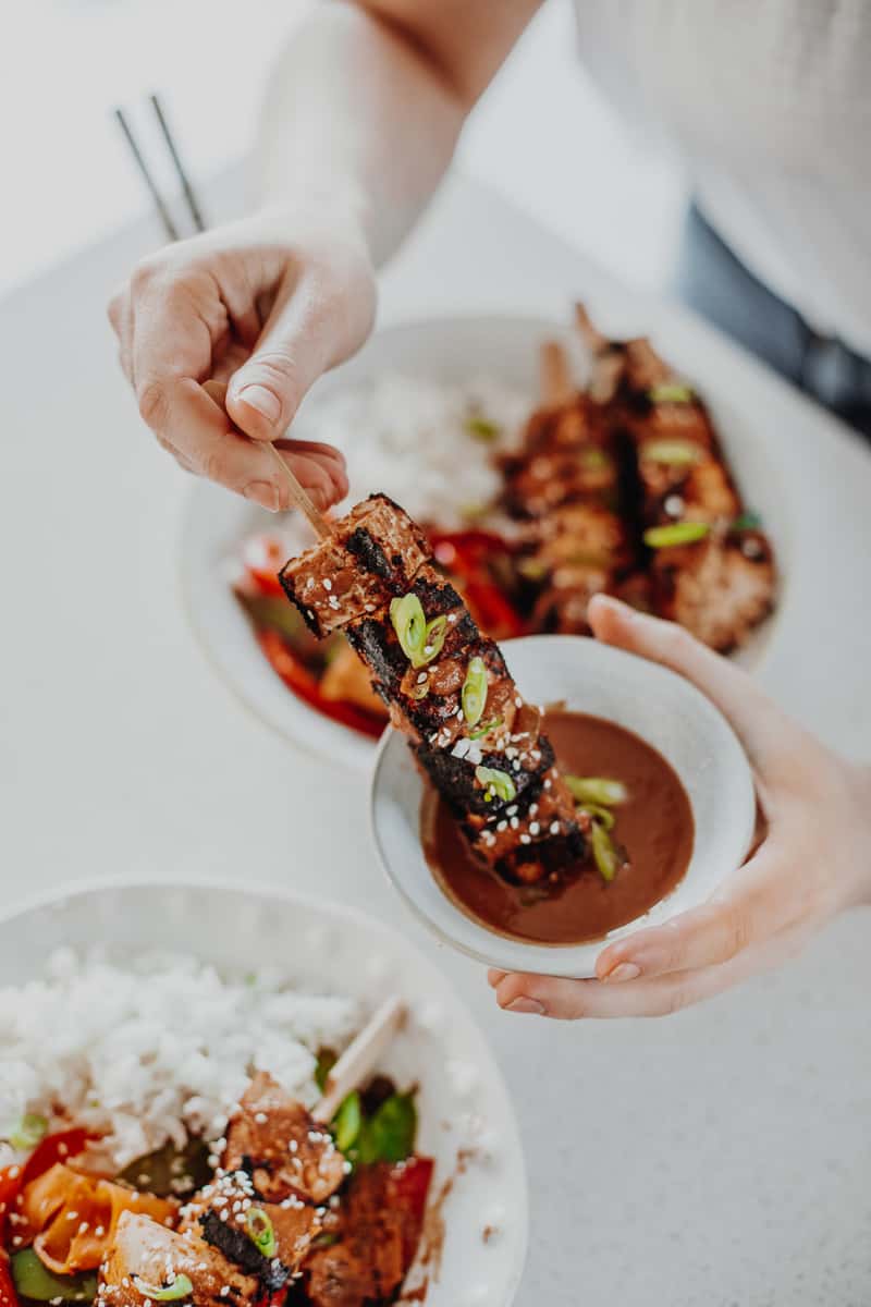 Dipping the satay tofu skewers in satay sauce.