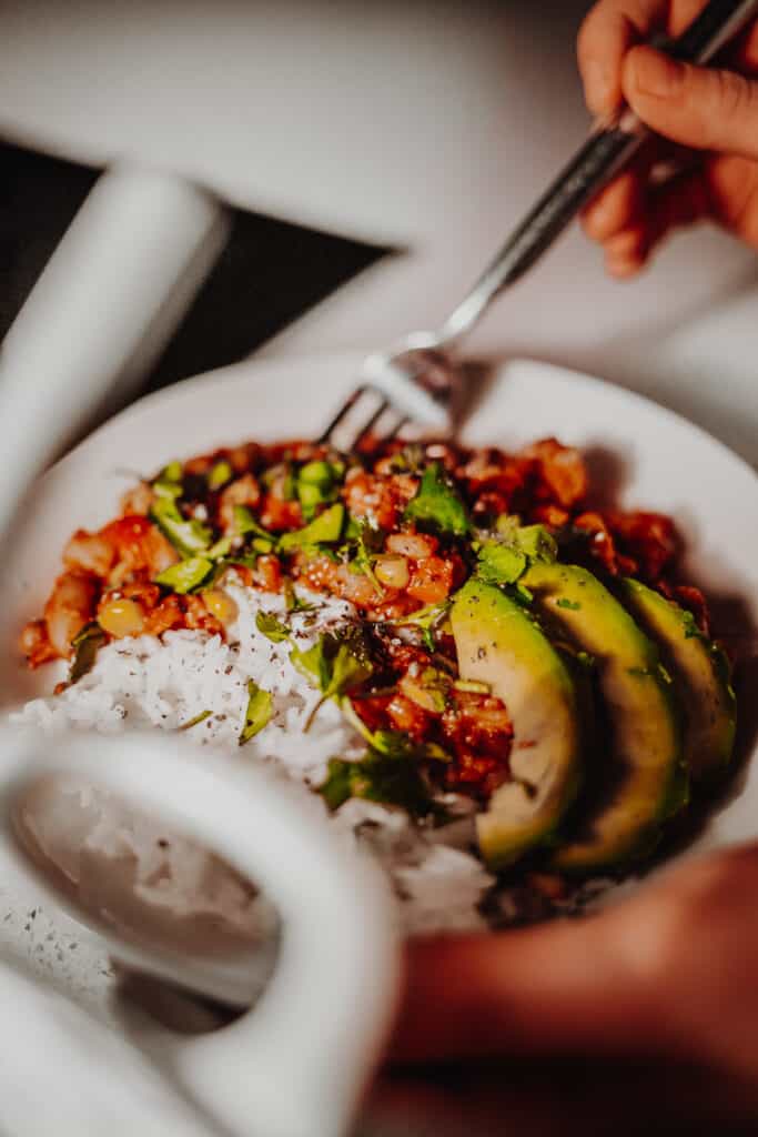 A bowl of Mixed-Bean Veggie Chilli with rice and avocado.