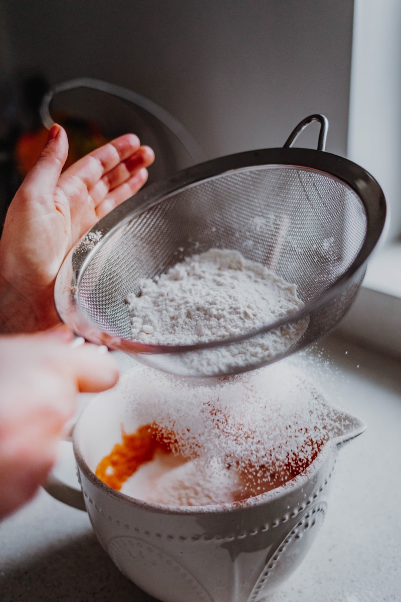 sifting the flour into the pumpkin puree batter
