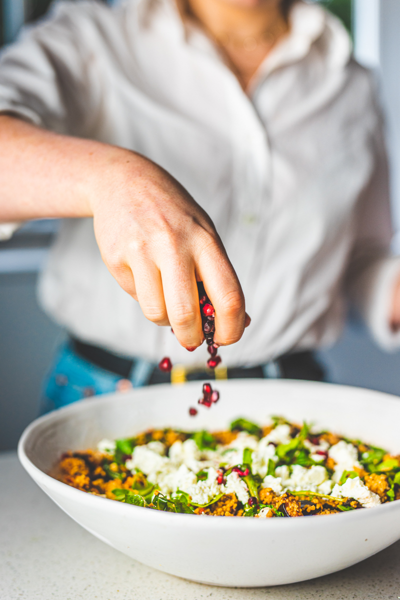 Sprinkling pomegranate seeds on Harissa Aubergine Salad - Georgie Eats