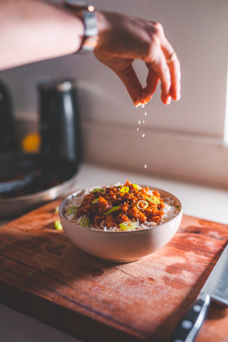 Sprinkling sesame seeds over Sticky Sesame Tofu - Georgie Eats