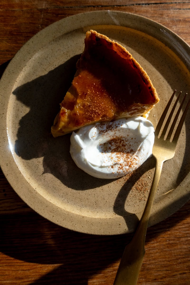 Warm slice of homemade pumpkin pie with whipped cream and cinnamon, served on a rustic plate.- Georgie Eats