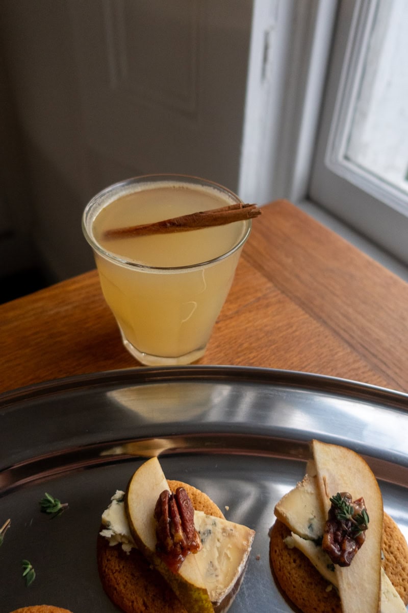 A warm apple toddy, garnished with a cinnamon stick next to a tray of canapes - Georgie Mullen